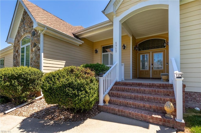 property entrance featuring a porch, a shingled roof, and stone siding
