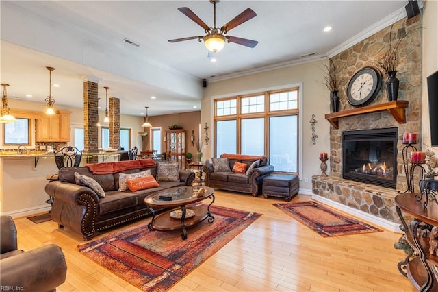 living room with crown molding, ceiling fan, light wood-style floors, a fireplace, and visible vents