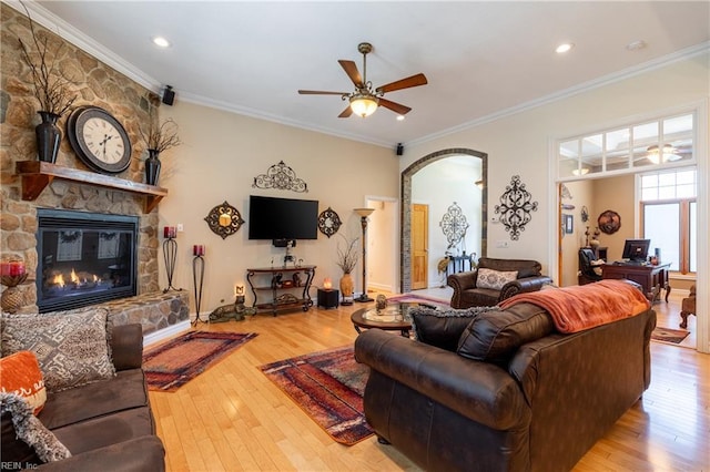 living room with wood-type flooring, a ceiling fan, arched walkways, and a stone fireplace