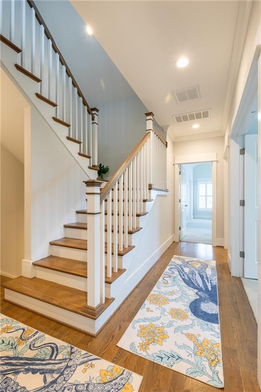 stairway with crown molding, baseboards, wood finished floors, and visible vents