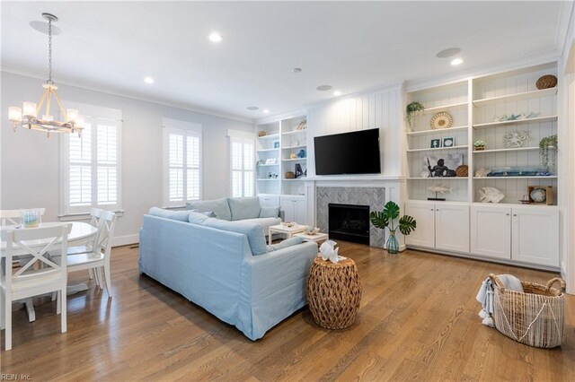 living area featuring crown molding, a notable chandelier, light wood-style flooring, and a fireplace