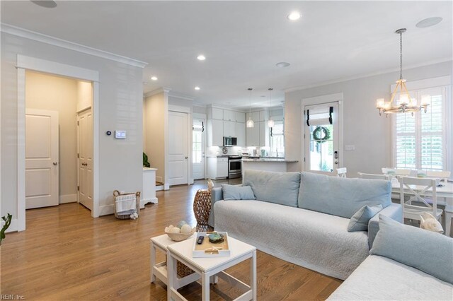 living room featuring a wealth of natural light, ornamental molding, light wood-type flooring, and a chandelier
