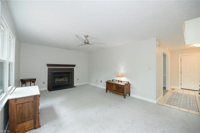 living room featuring a fireplace with flush hearth, baseboards, a ceiling fan, and light colored carpet