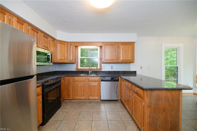 kitchen with a peninsula, brown cabinets, tasteful backsplash, a sink, and appliances with stainless steel finishes