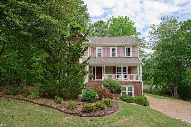 view of front of property featuring a porch, brick siding, a front lawn, concrete driveway, and stairs