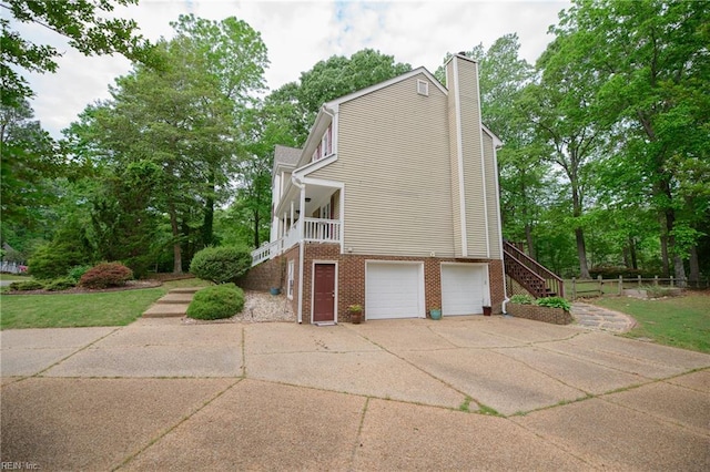view of side of property featuring a chimney, stairs, brick siding, an attached garage, and driveway