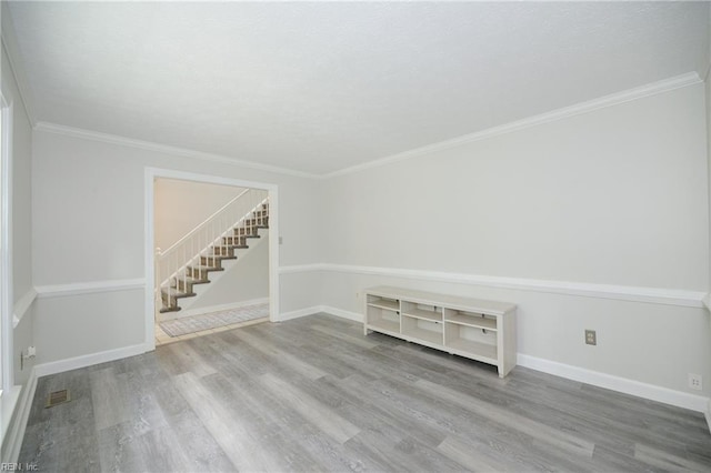 spare room with crown molding, stairs, baseboards, wood finished floors, and visible vents