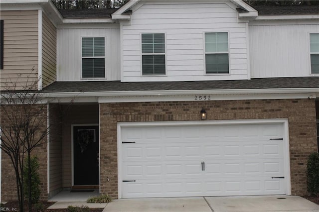 view of front of property featuring roof with shingles, an attached garage, concrete driveway, and brick siding
