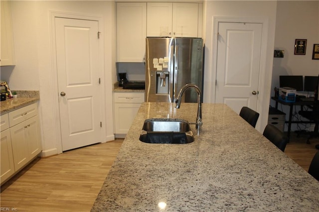kitchen featuring stainless steel refrigerator with ice dispenser, white cabinetry, a sink, and light wood-style floors