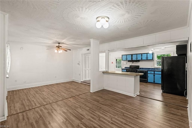 kitchen featuring dark wood-style flooring, a ceiling fan, a peninsula, black appliances, and blue cabinets