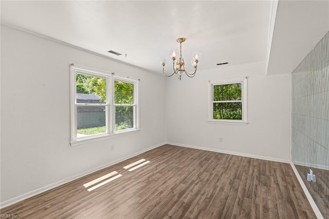 unfurnished room with baseboards, an inviting chandelier, wood finished floors, and visible vents