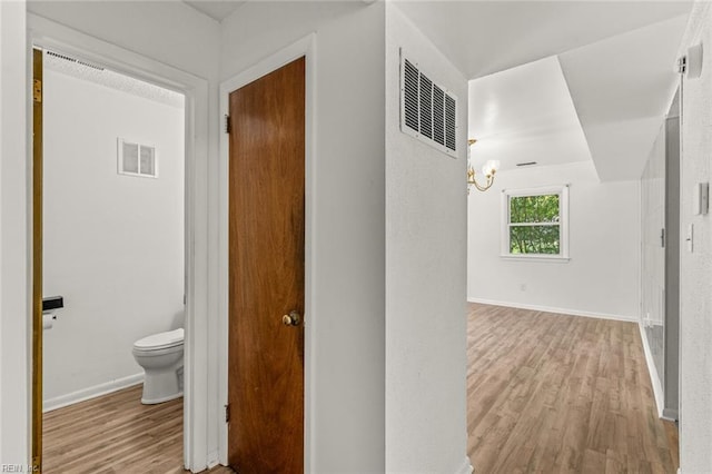 hall featuring baseboards, wood finished floors, and visible vents