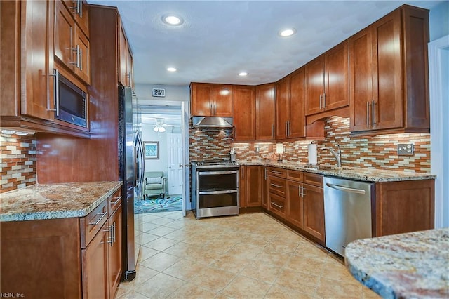 kitchen featuring under cabinet range hood, backsplash, appliances with stainless steel finishes, and light stone counters