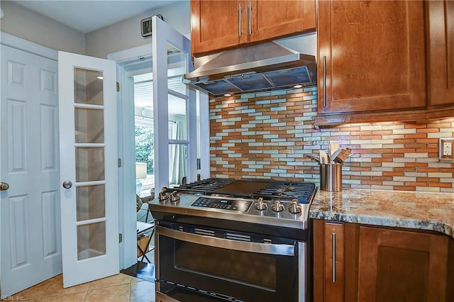 kitchen featuring light tile patterned floors, stainless steel range with gas stovetop, ventilation hood, and decorative backsplash