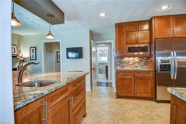 kitchen with brown cabinetry, pendant lighting, light stone counters, a sink, and appliances with stainless steel finishes