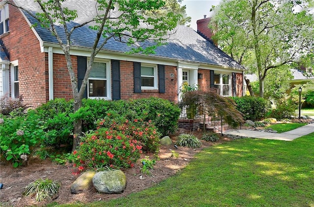 cape cod-style house with brick siding, a chimney, and a front yard