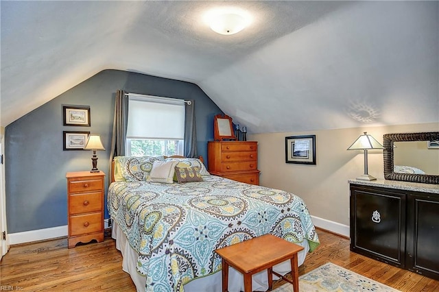 bedroom featuring baseboards, wood finished floors, and lofted ceiling