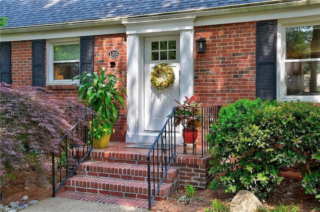 property entrance featuring a shingled roof and brick siding