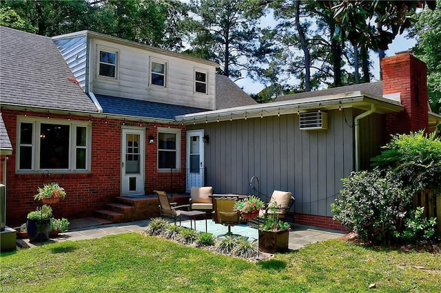 rear view of house featuring roof with shingles, brick siding, a chimney, a lawn, and a patio
