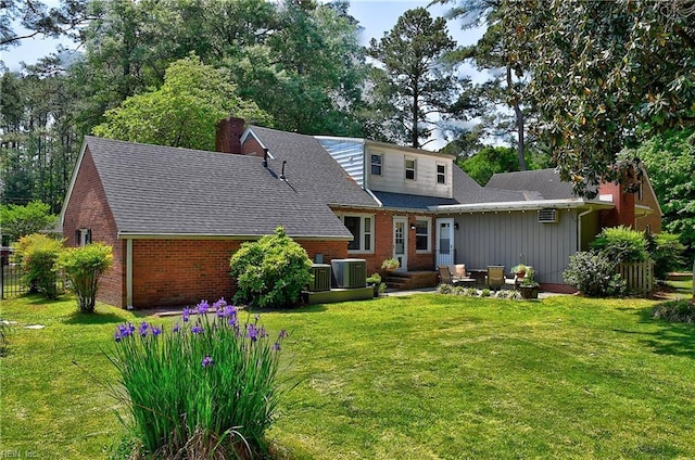 back of property featuring a chimney, brick siding, a shingled roof, central air condition unit, and a yard