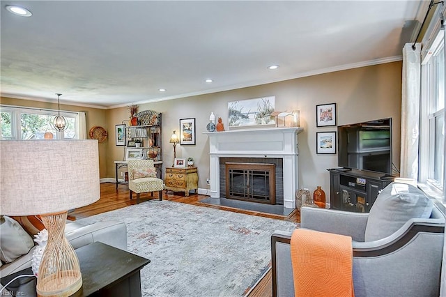 living room featuring a brick fireplace, recessed lighting, ornamental molding, and wood finished floors
