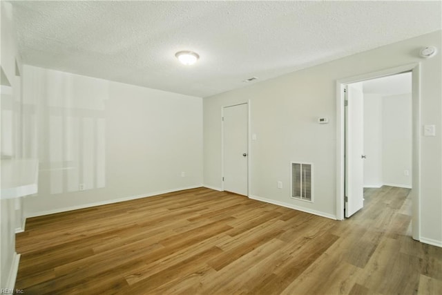 empty room featuring visible vents, baseboards, a textured ceiling, and wood finished floors