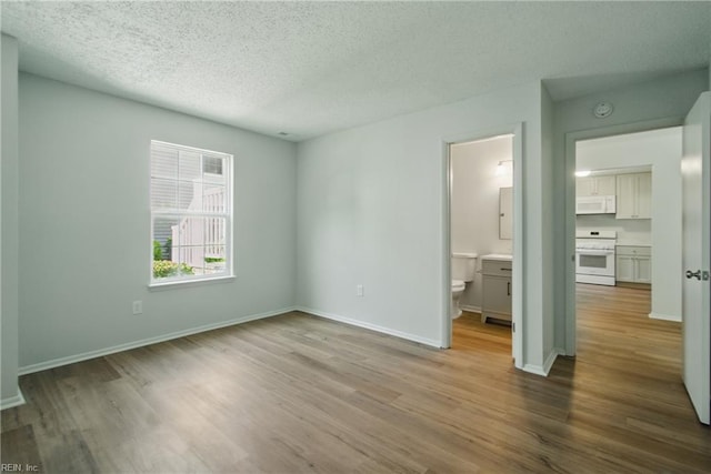 unfurnished bedroom with baseboards, connected bathroom, a textured ceiling, and wood finished floors