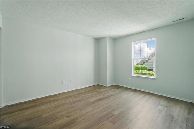 spare room featuring baseboards, a textured ceiling, visible vents, and wood finished floors