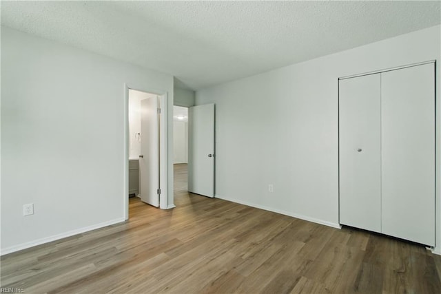 unfurnished bedroom featuring baseboards, a textured ceiling, wood finished floors, and a closet