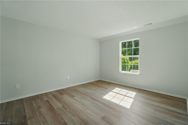 empty room with a textured ceiling, baseboards, visible vents, and wood finished floors