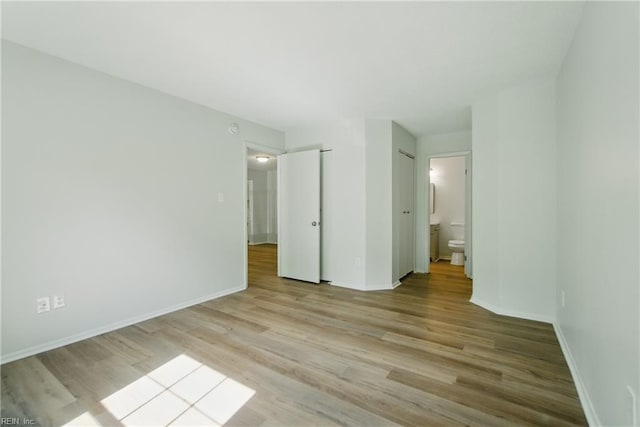 unfurnished bedroom with light wood-style floors, baseboards, and ensuite bath