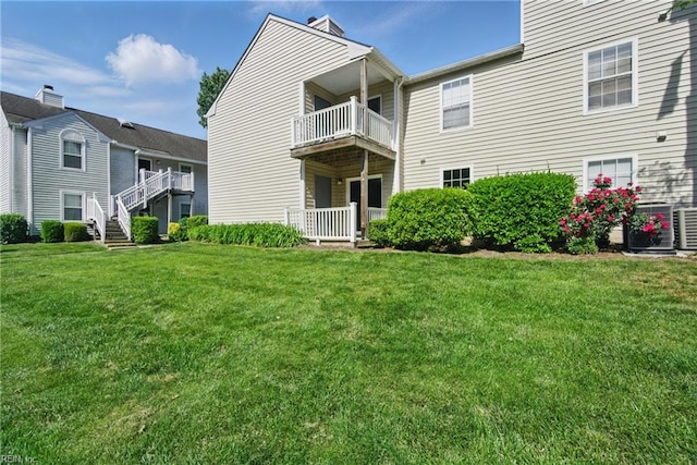 back of property with a lawn, central air condition unit, a chimney, and a balcony
