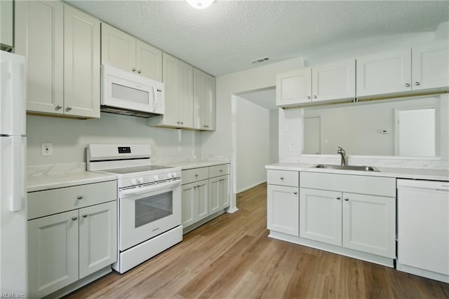 kitchen featuring visible vents, white appliances, light countertops, a sink, and light wood-style flooring