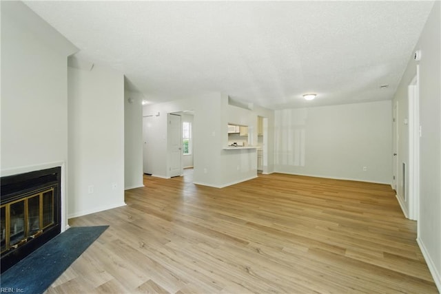 unfurnished living room with a fireplace with flush hearth, baseboards, light wood finished floors, and a textured ceiling