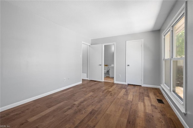 unfurnished bedroom featuring baseboards, dark wood-style flooring, ensuite bathroom, and visible vents
