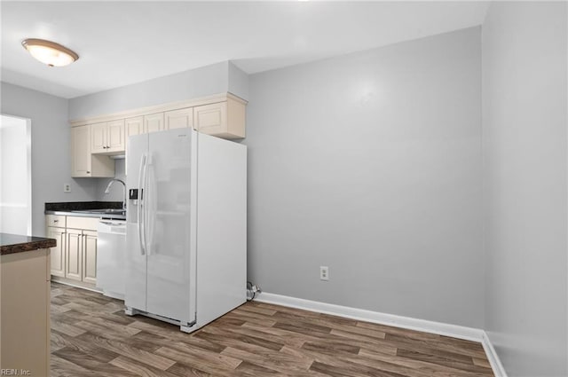 kitchen with dark countertops, dark wood finished floors, a sink, baseboards, and white appliances