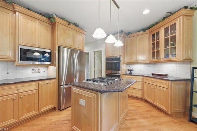 kitchen with a kitchen island, appliances with stainless steel finishes, light wood-type flooring, glass insert cabinets, and dark stone counters