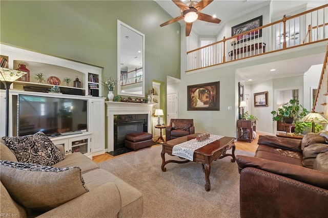 living area with a glass covered fireplace, ceiling fan, wood finished floors, and a towering ceiling