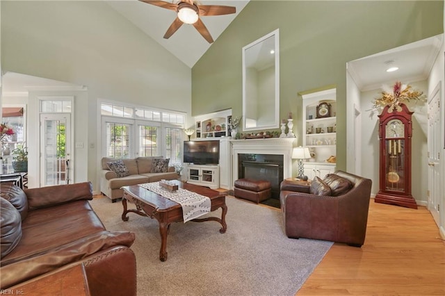 living room with a glass covered fireplace, wood finished floors, baseboards, high vaulted ceiling, and a ceiling fan