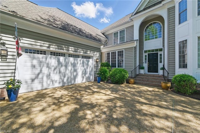property entrance featuring driveway, a shingled roof, and a garage
