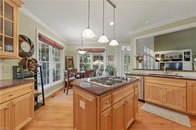 kitchen with a sink, dark stone countertops, light wood-style floors, ornamental molding, and stainless steel appliances