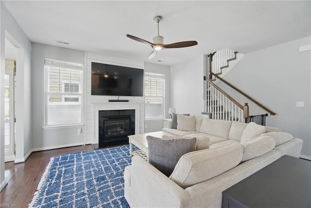 living area featuring ceiling fan, baseboards, wood finished floors, visible vents, and stairway