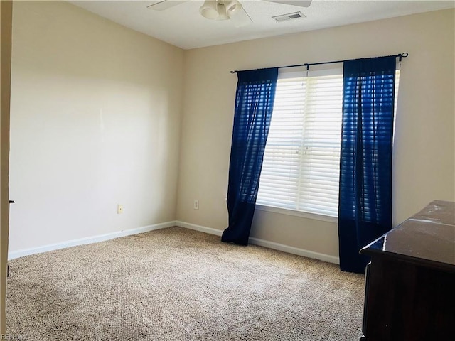 empty room featuring plenty of natural light, a ceiling fan, visible vents, carpet floors, and baseboards