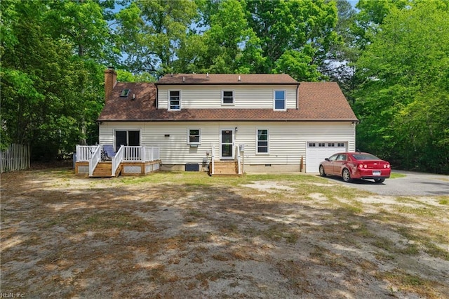 rear view of house featuring a chimney, an attached garage, a deck, and aphalt driveway