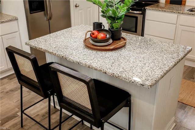 interior details with a center island, light wood-style flooring, a kitchen breakfast bar, and white cabinetry