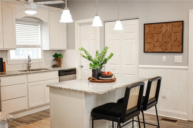 kitchen featuring visible vents, wood finished floors, a kitchen bar, a sink, and dishwasher