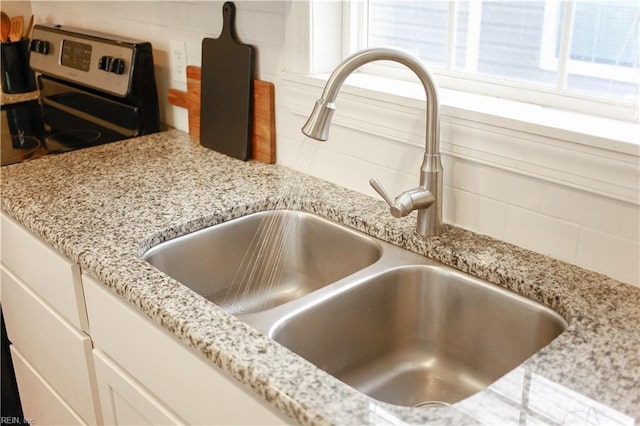 interior details featuring tasteful backsplash, stainless steel range with electric cooktop, a sink, light stone counters, and white cabinetry