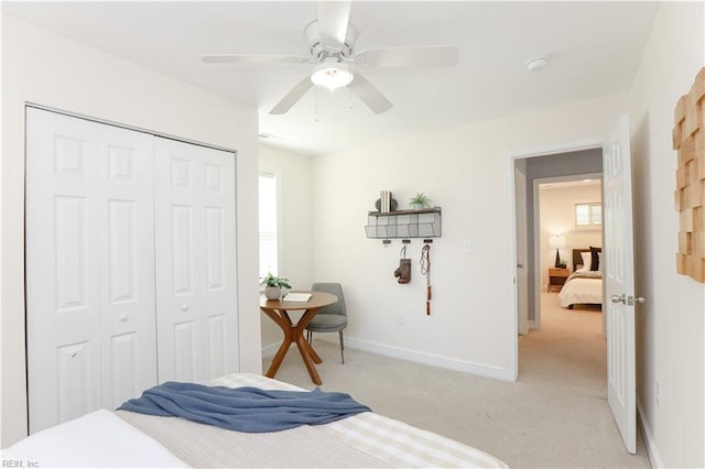 bedroom with baseboards, a ceiling fan, a closet, and light colored carpet