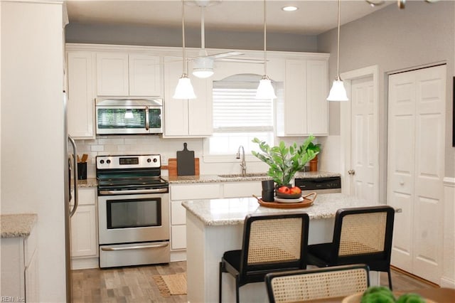 kitchen with decorative backsplash, a sink, light wood-style floors, stainless steel appliances, and white cabinetry