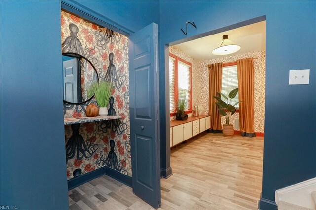 corridor featuring baseboards, wallpapered walls, and light wood-style flooring
